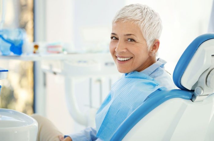 Older woman with perfect teeth smiling over her shoulder worn teeth dentist in New Bern North Carolina